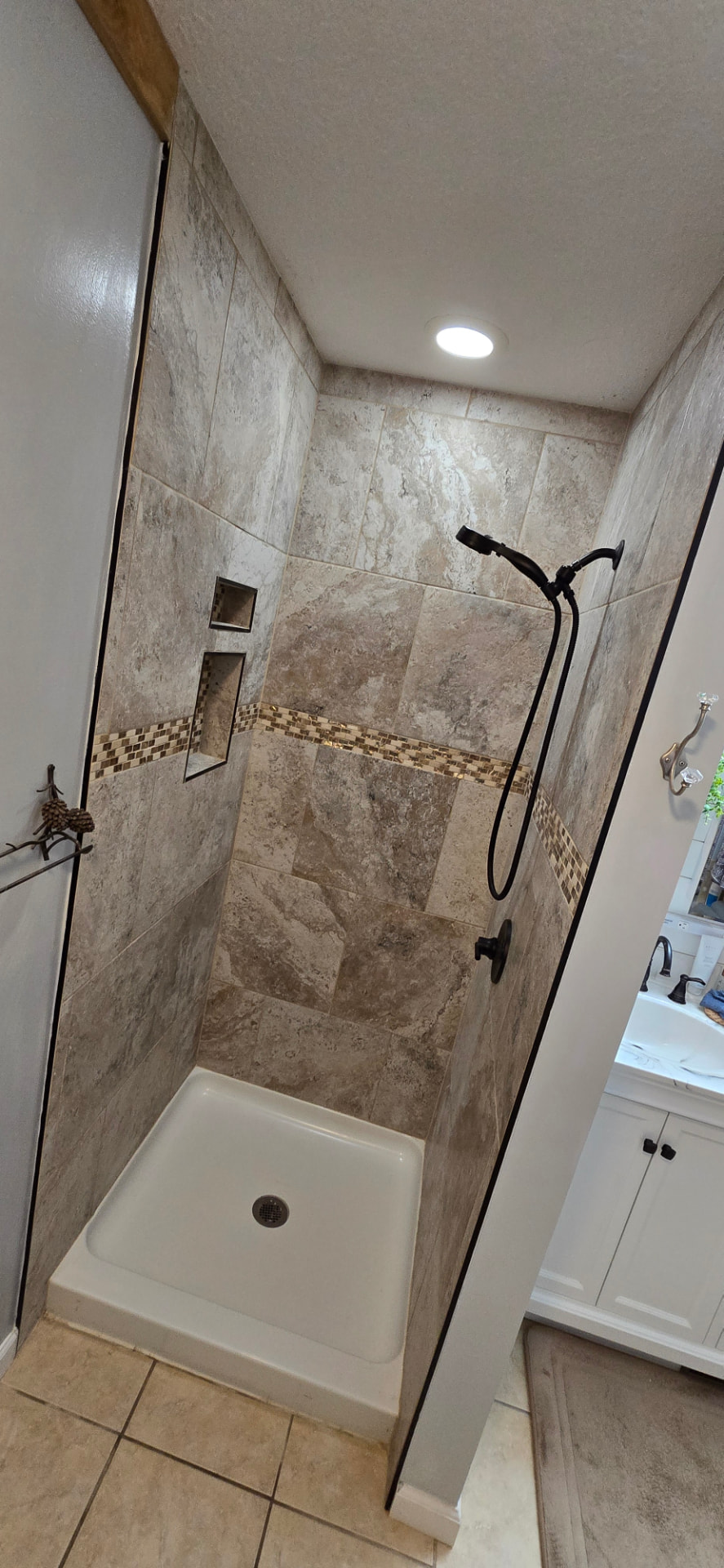 Finished travertine-look tile shower with mosaic accent band, double niche, and oil-rubbed bronze fixtures