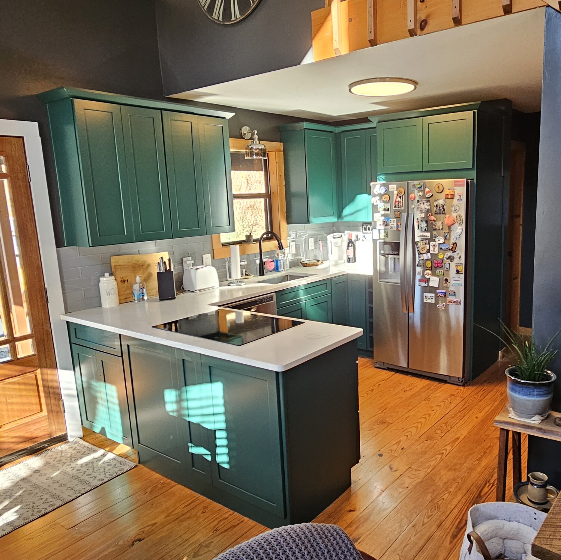 Remodeled kitchen with deep green shaker cabinets, white quartz countertops, subway tile backsplash, and refinished pine floors